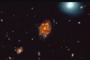 This JWST image shows the Big Wheel galaxy (in the center) and its cosmic environment. The galaxy is a gigantic rotating disk lying 11.7 billion light-years away. Its spiral disk stretches across 100,000 light-years, making it larger than any other galaxy disk confirmed at this epoch of the universe. The blue blob and some of the other larger objects in the image are galaxies in the nearby universe. The smaller objects tend to be distant galaxies; however, the larger galaxy to the lower left of Big Wheel is part of the same remote galactic structure as Big Wheel. Credit: NASA/ESA